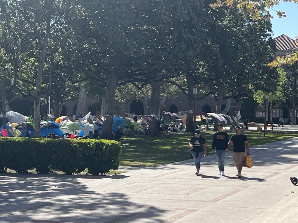 Three students walk past tents on Trousdale Parkway