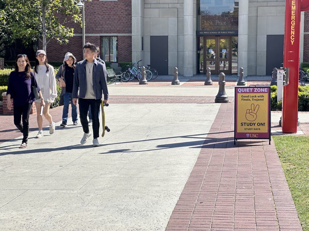 Four USC students walk behind a path between Doheny library and the Alumni House